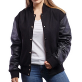 A woman wearing a black varsity jacket with leather sleeves and a wool body, buttoned at the front with metal buttons, standing against a white background.