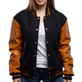 A woman wearing a black and orange varsity jacket with leather sleeves and wool body, buttoned at the front with metal buttons, standing against a white background.