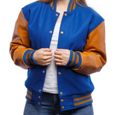 A woman wearing a blue and brown varsity jacket with leather sleeves and wool body, buttoned up with metal buttons.