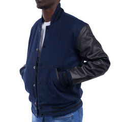 A man wearing a navy blue varsity jacket with black leather sleeves and a collar, standing against a white background.