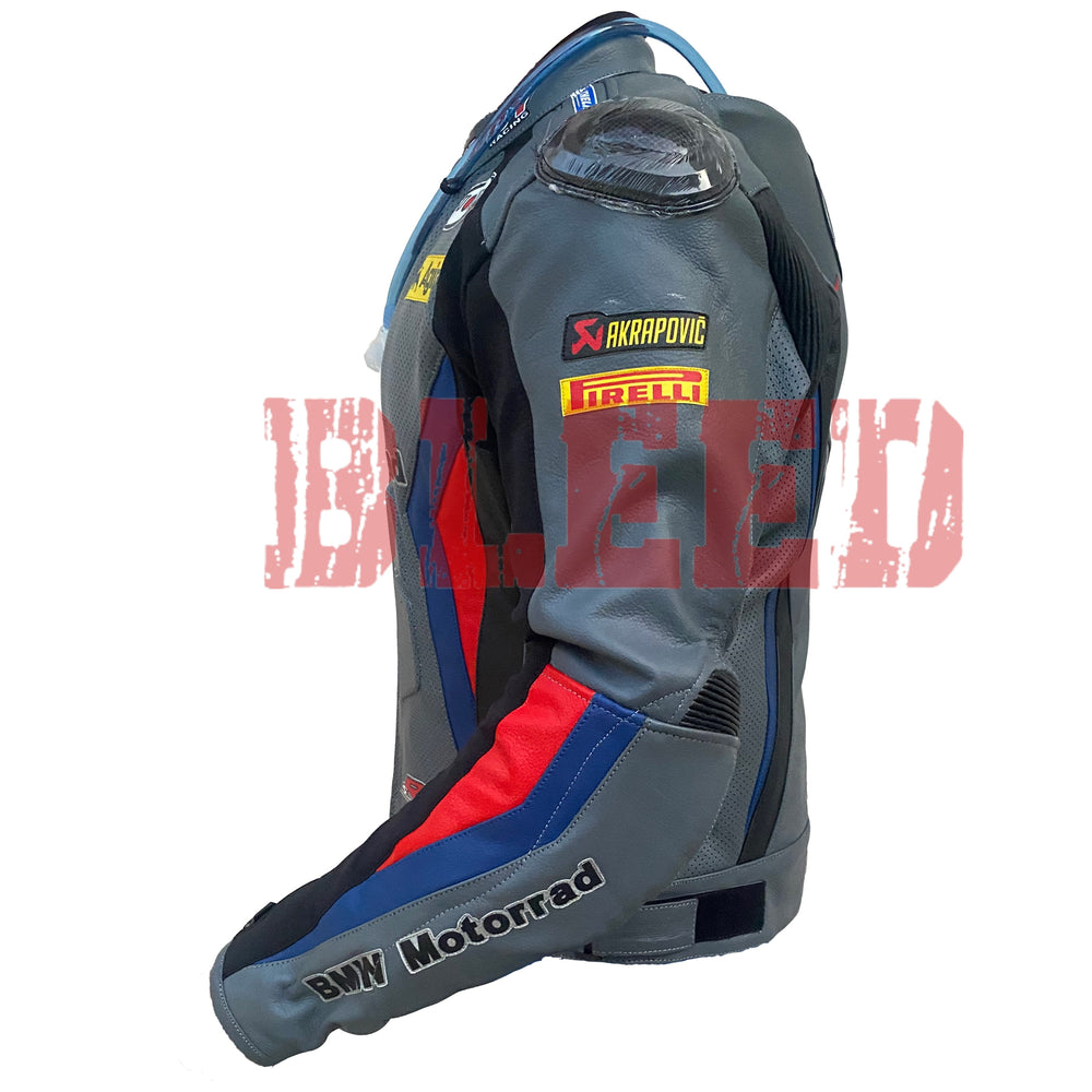 Left side view of the BMW Motorrad Racing Motorcycle Jacket. The gray leather jacket features sponsor logos including Akrapovic and Pirelli on the sleeve, with red and blue accents along the arm. The 'BMW Motorrad' branding is prominently displayed on the forearm, highlighting the jacket's racing-inspired design