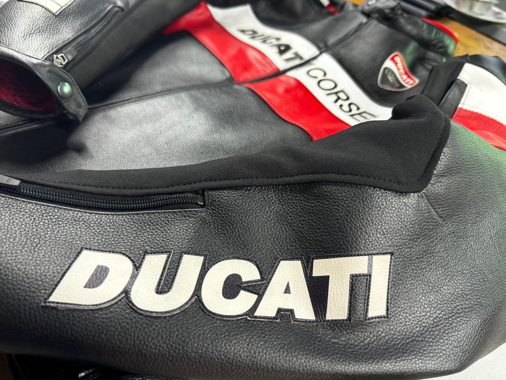 Close-up of the Ducati Corse C5 Men's Motorcycle Leather Jacket, showcasing the black leather texture and prominent 'Ducati' branding. The image highlights the jacket's red, white, and black color scheme and detailed craftsmanship