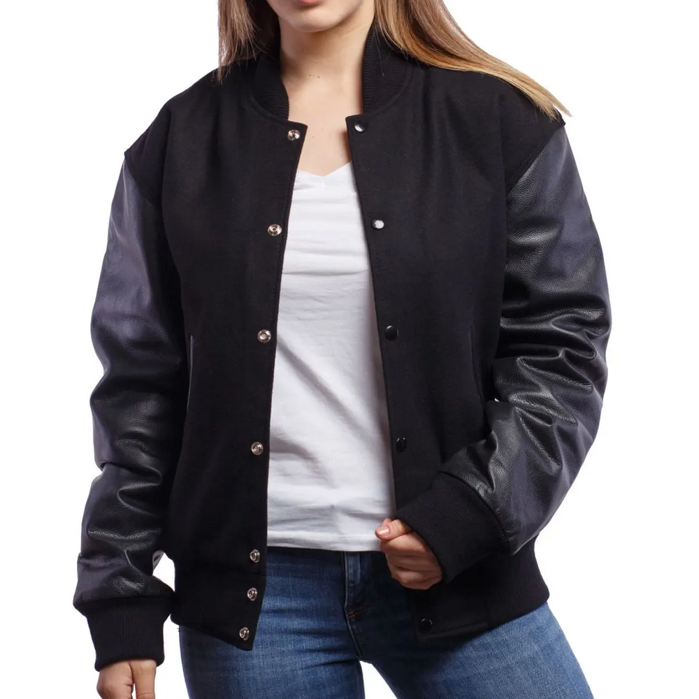 A woman wearing a black varsity jacket with leather sleeves and a wool body, buttoned at the front with metal buttons, standing against a white background.