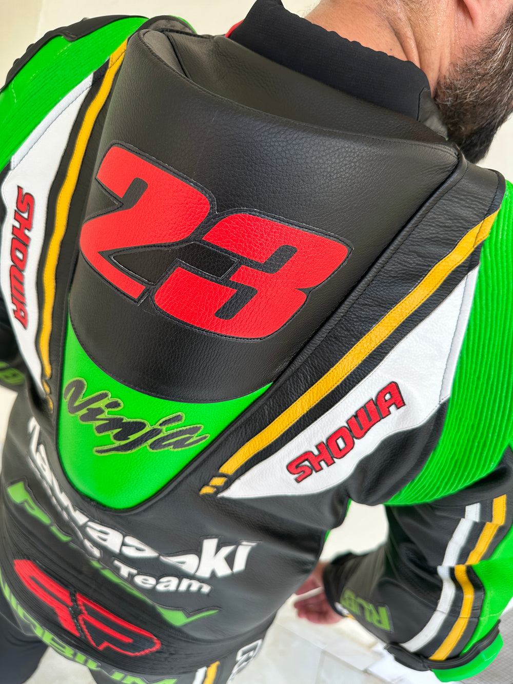 Closeup view of the Kawasaki Racing Team suit. High-performance Kawasaki Racing Team motorcycle suit with a sleek black design, vibrant green and white highlights, and prominent sponsor logos such as Provec and Ninja.