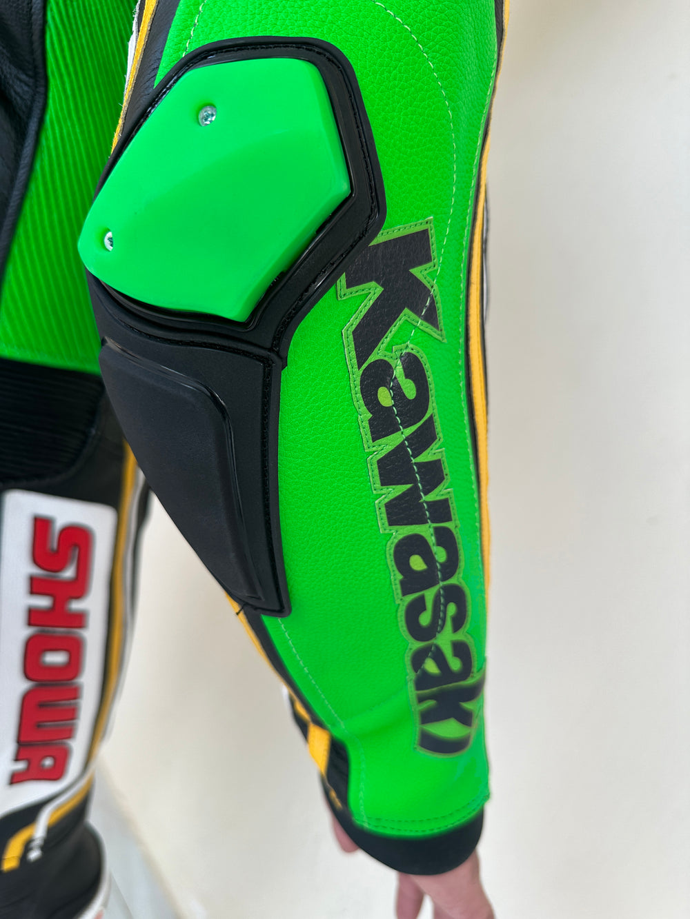 Closeup view of the Kawasaki Racing Team suit. High-performance Kawasaki Racing Team motorcycle suit with a sleek black design, vibrant green and white highlights, and prominent sponsor logos such as Provec and Ninja.