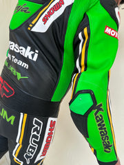 Closeup view of the Kawasaki Racing Team suit. High-performance Kawasaki Racing Team motorcycle suit with a sleek black design, vibrant green and white highlights, and prominent sponsor logos such as Provec and Ninja.